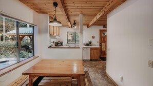 A modern kitchen with wooden beams, a large window, and a dining area with a wooden table and benches. - 67MF- Hot Tub - Pets Ok - BBQ - Sleeps 5 (Maple Falls)