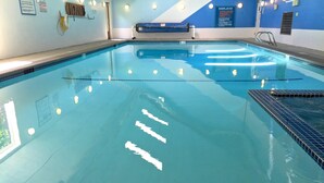 A clear indoor swimming pool with tiled walls, a pool ladder, and a pool deck.