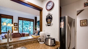 A kitchen with a stainless steel refrigerator, a coffee maker, and a toaster on the counter. There is a sink and a window with a view of trees.
