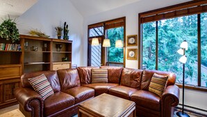 A spacious living room with a brown leather sectional sofa, a wooden coffee table, and a bookshelf filled with books and decorative items.