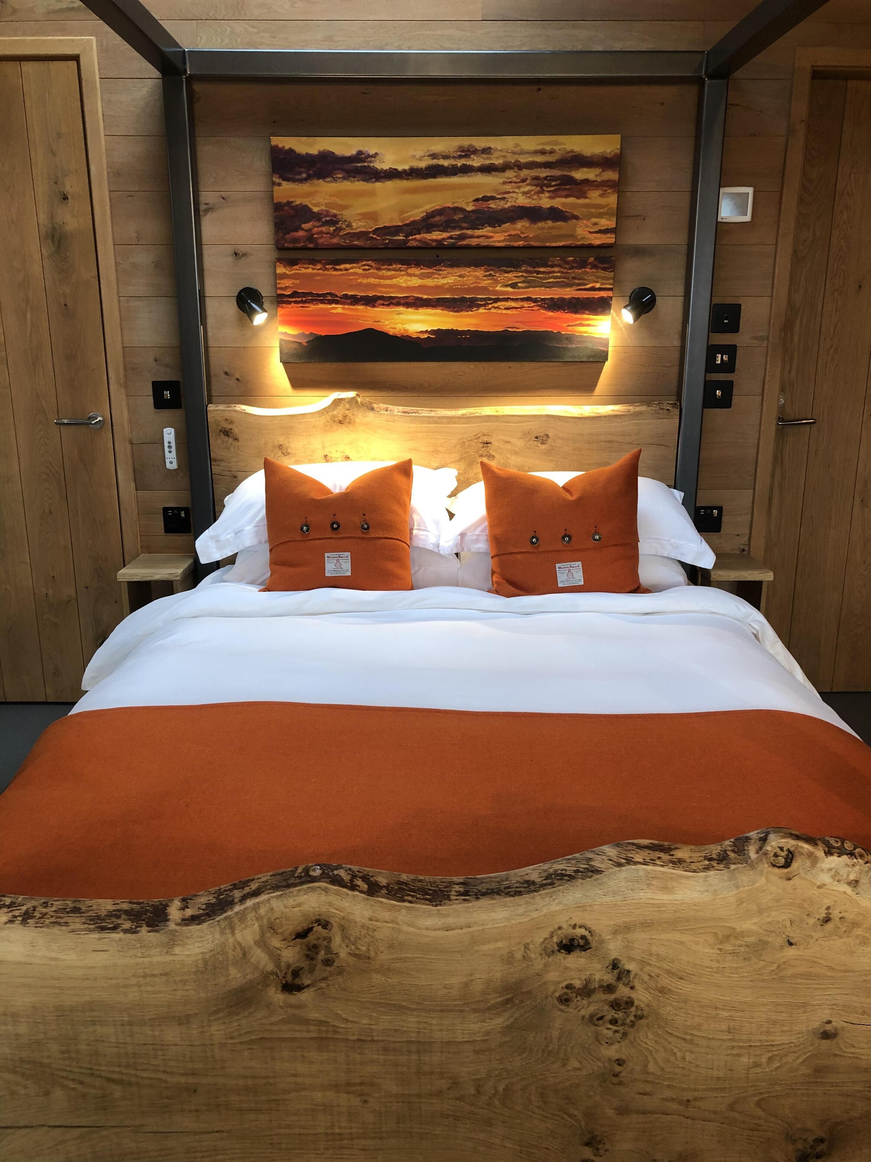 A bedroom with a wooden headboard, a large painting of a sunset, and two nightstands with lamps.