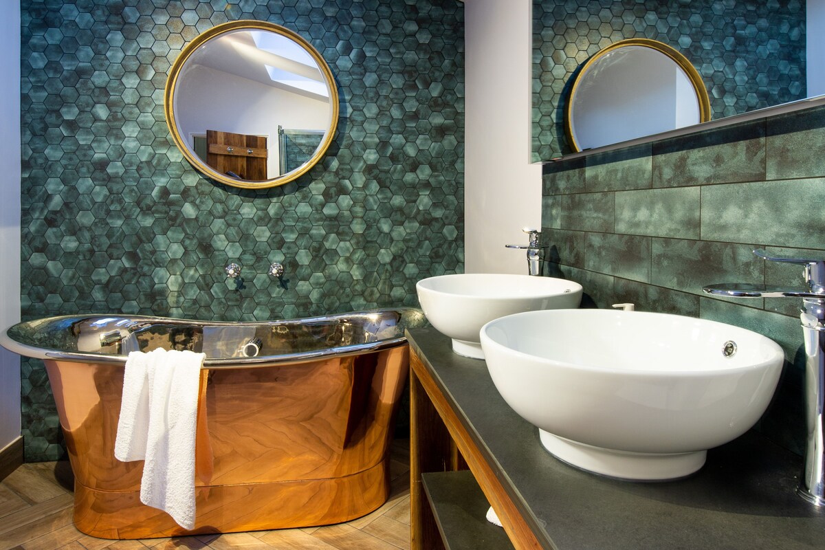 Un baño moderno con una bañera independiente, dos lavamanos y un espejo grande.