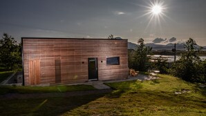 A modern, single-story building with a wooden exterior, a black door, and a small window. - Ardcana (Strath)