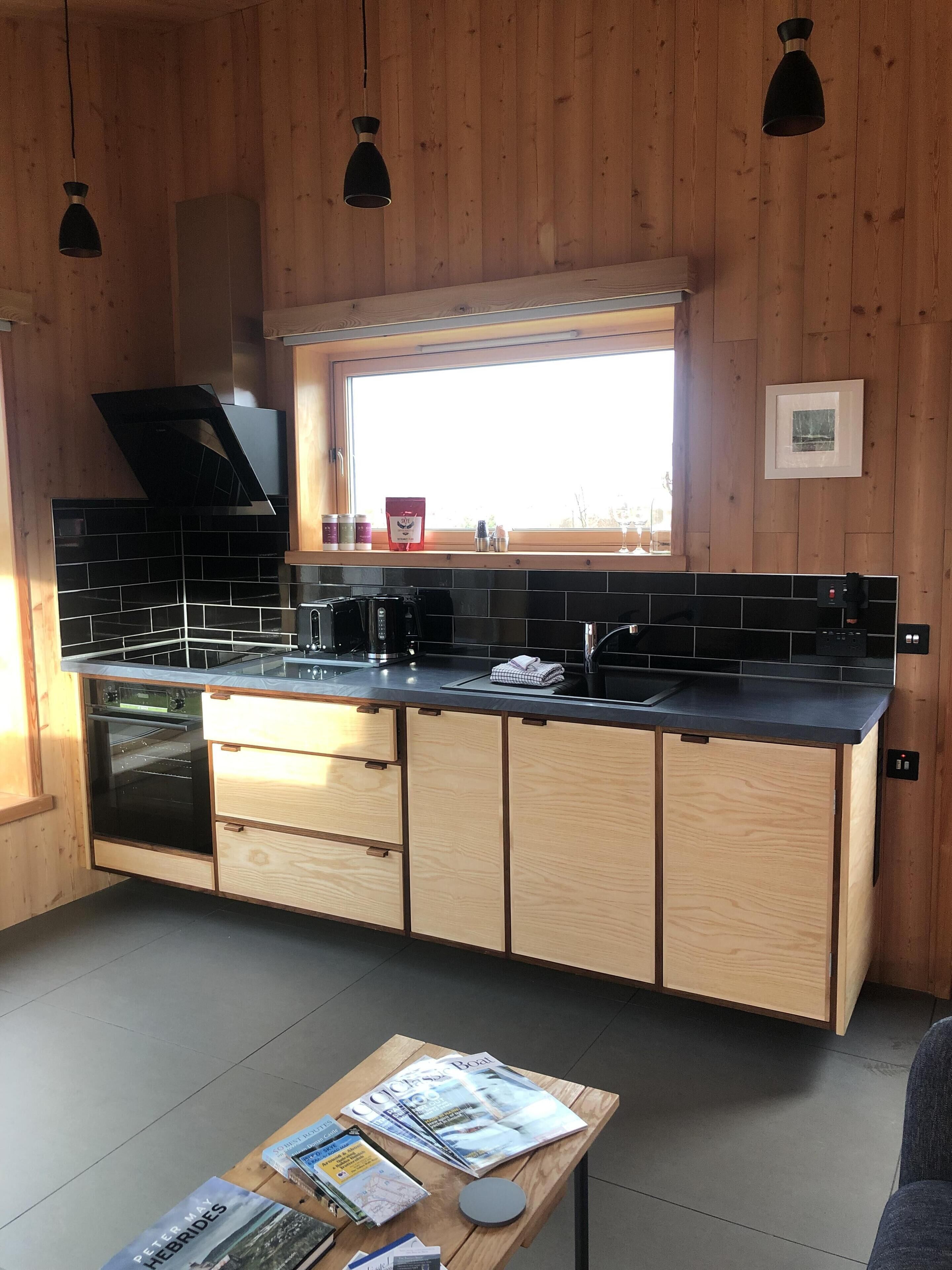 A modern kitchen with wooden cabinets, a black countertop, and a window above the sink.