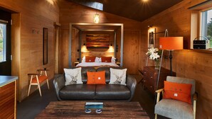 A cozy cabin interior with a wooden interior, a bed with orange pillows, a leather sofa, a wooden coffee table, and a desk with a lamp. - Ardcana (Strath)