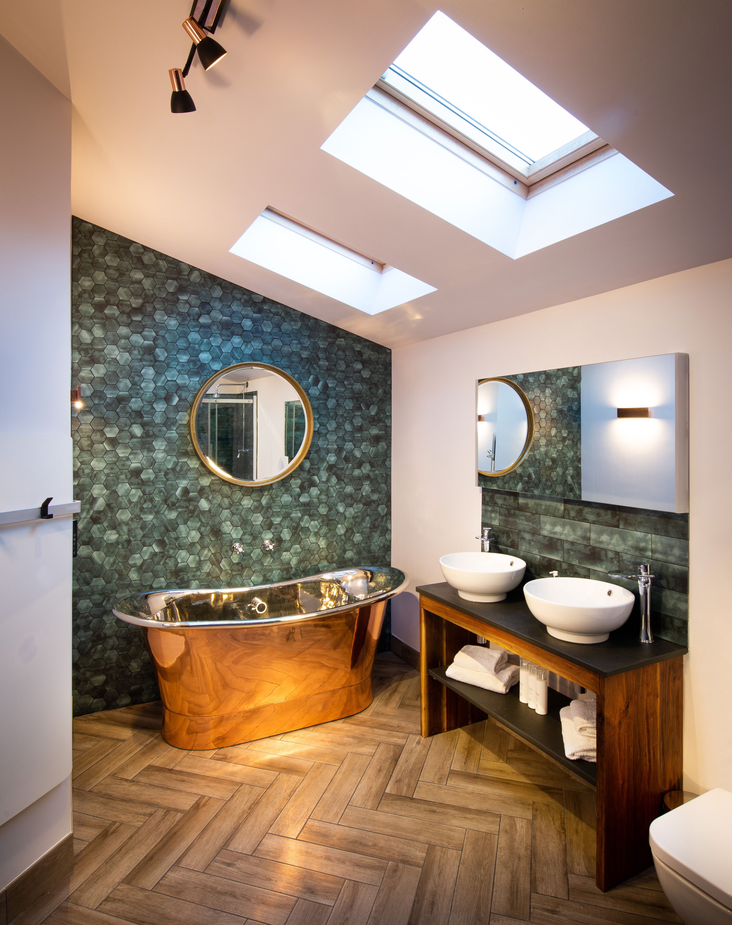 Ein modernes Badezimmer mit einer freistehenden Badewanne, zwei Waschbecken, einem großen Spiegel und einem Dachfenster.