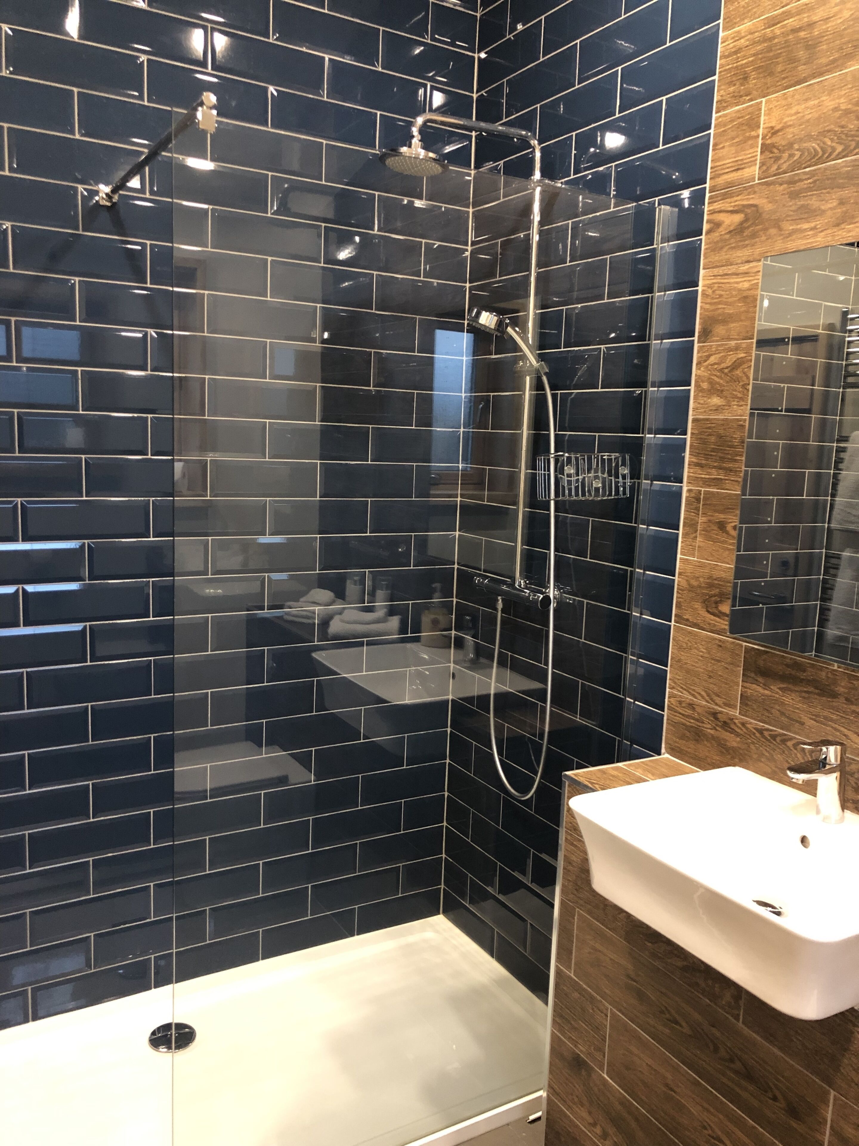 Un baño moderno con paredes de azulejos negros, una ducha y un lavabo blanco.