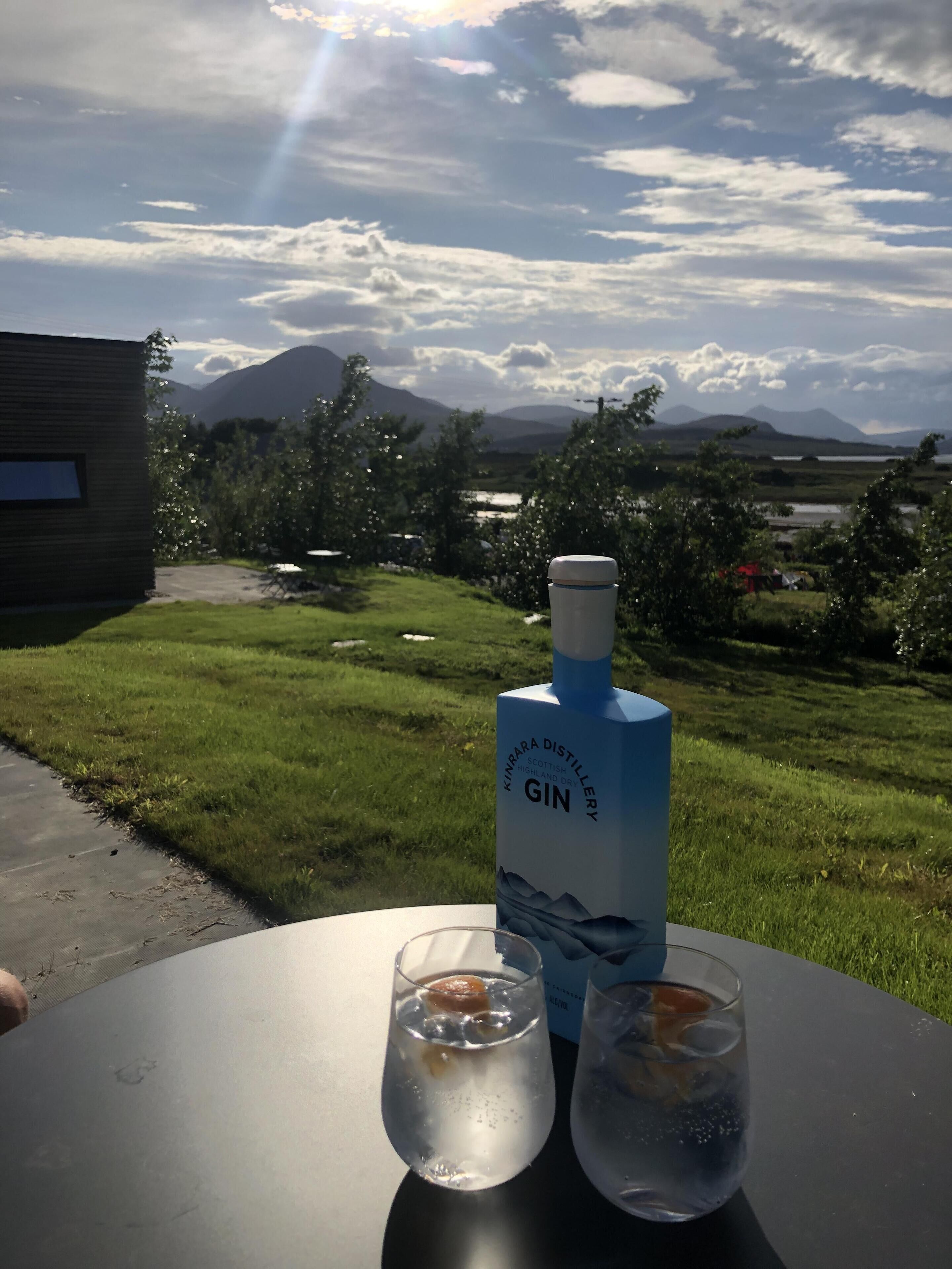 A bottle of gin and two glasses on a table with a scenic outdoor view.