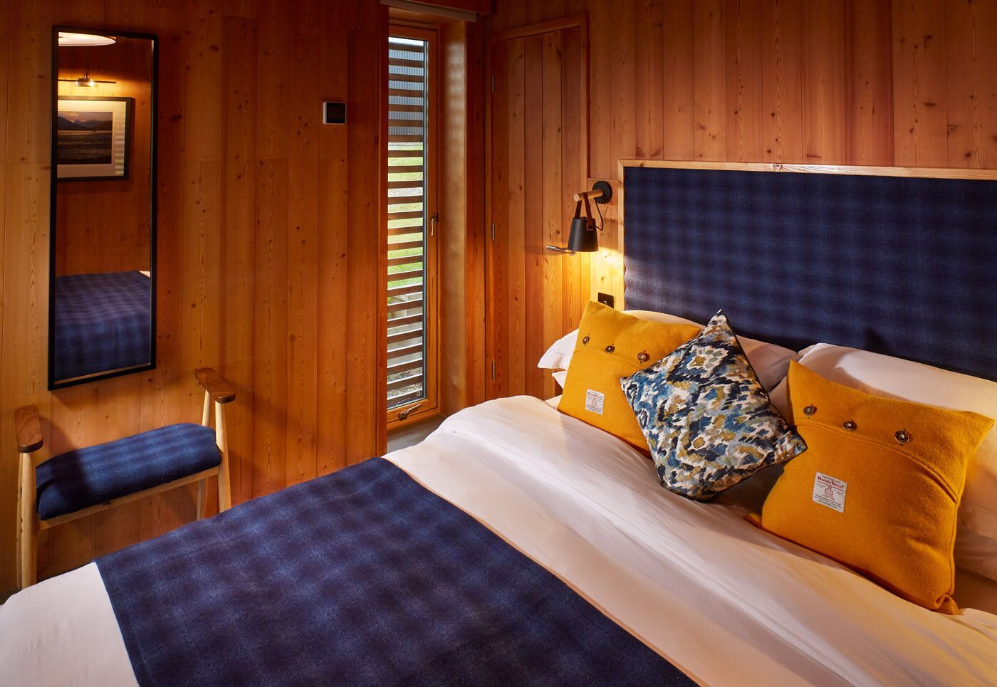 A wooden-paneled room with a bed, a chair, and a window with blinds.
