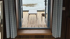 A wooden deck with a table and chairs, leading to a view of a lake and mountains. - Ardcana (Strath)