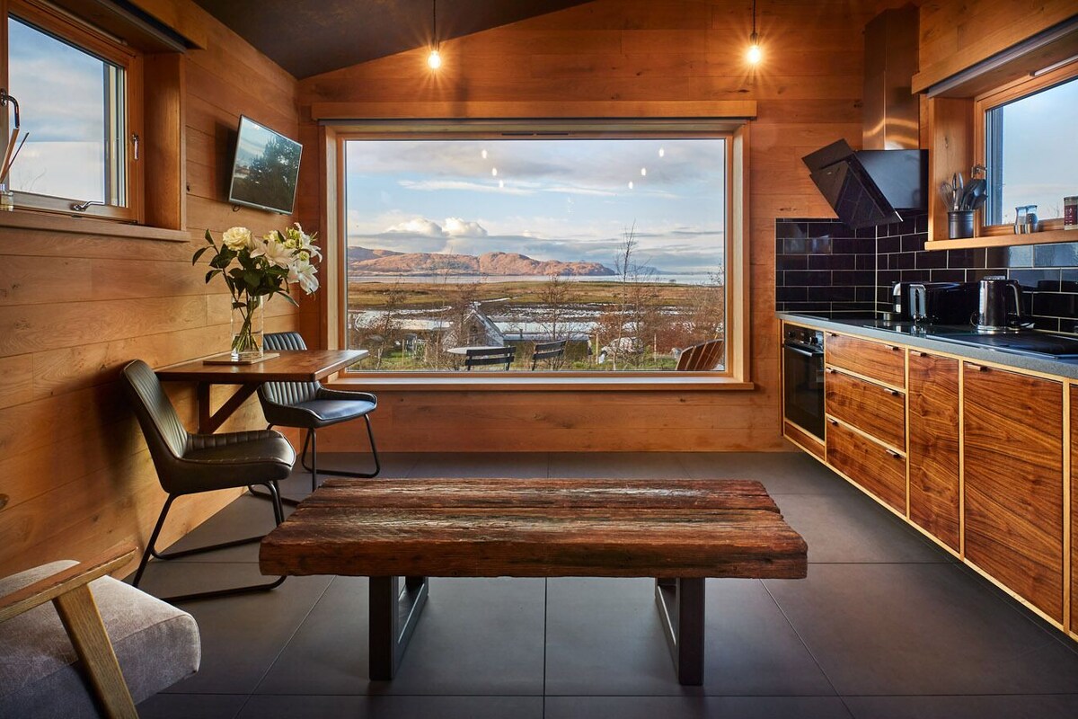 Una cocina moderna con un ventanal amplio, armarios de madera y un banco en el centro.