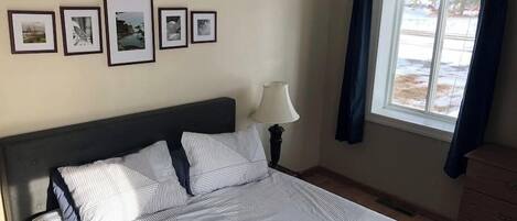 Une chambre à coucher avec un lit, une table de chevet avec une lampe, une commode et une fenêtre avec des rideaux.