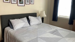Un letto ben rifatto con lenzuola a righe, una testiera scura e una lampada fissata al muro.
