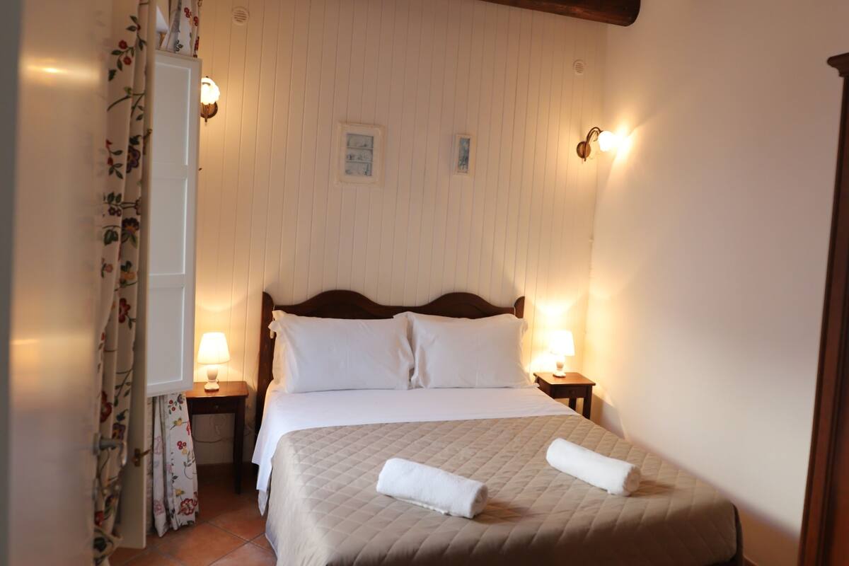 A neatly made bed with white linens, a wooden headboard, and two bedside lamps.