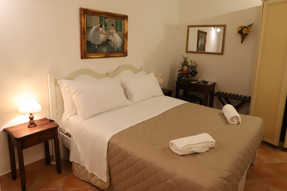 A neatly made bed with a brown blanket, a bedside table with a lamp, and a painting on the wall.