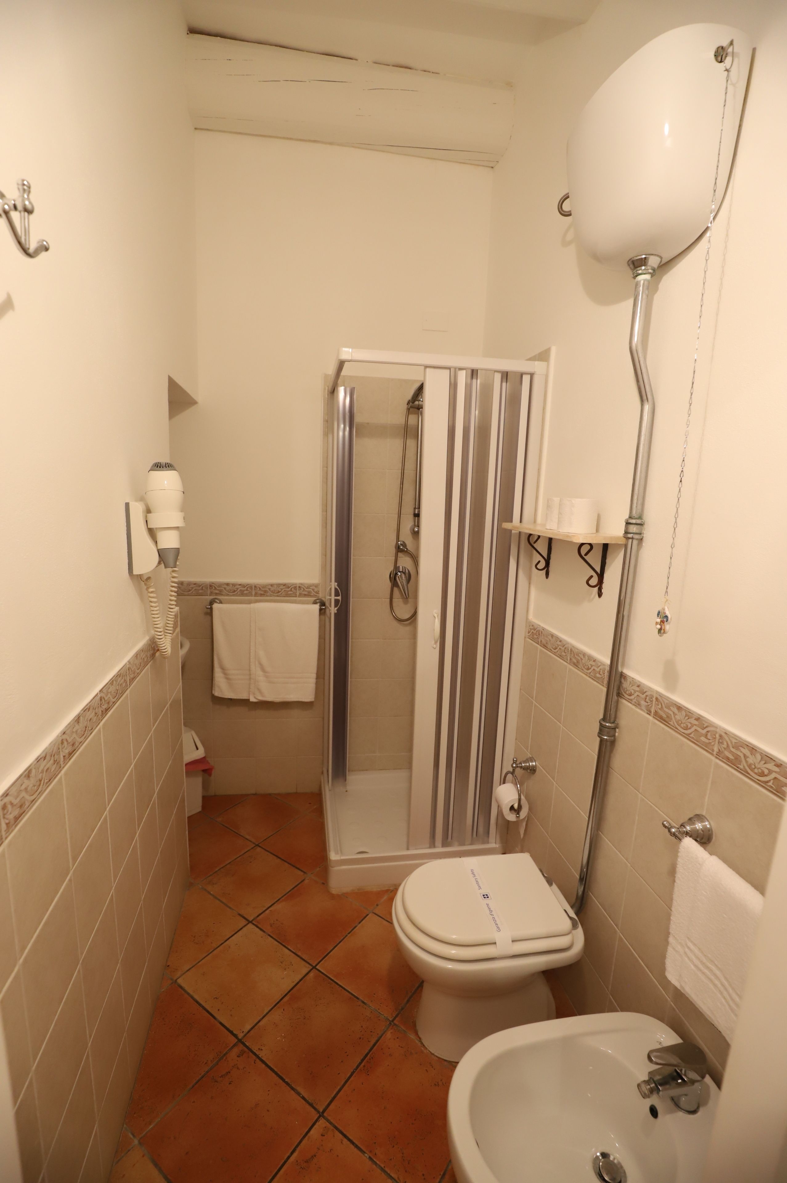 Badeværelse med brusebad, toilet, bidet og en hårtørrer på væggen.