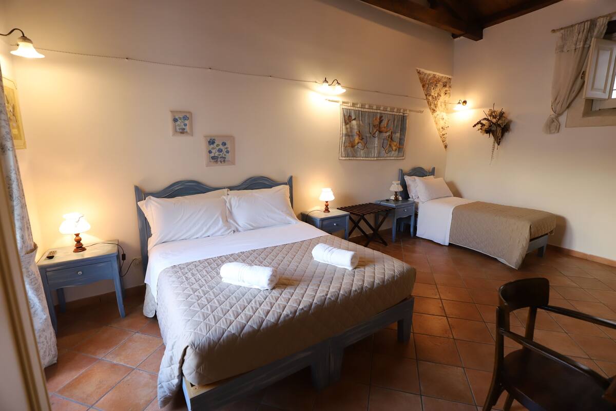 A bedroom with two beds, a nightstand with a lamp, a small table, and a chair.