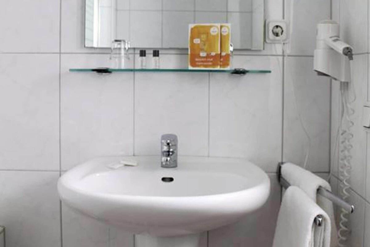 A bathroom with a white sink, a glass shelf with toiletries, and a towel rack.