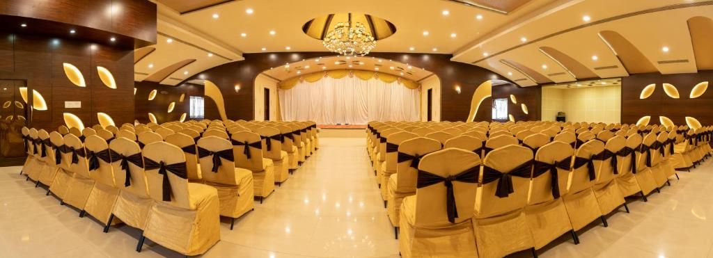 A conference room with rows of chairs, a stage with curtains, and a chandelier.
