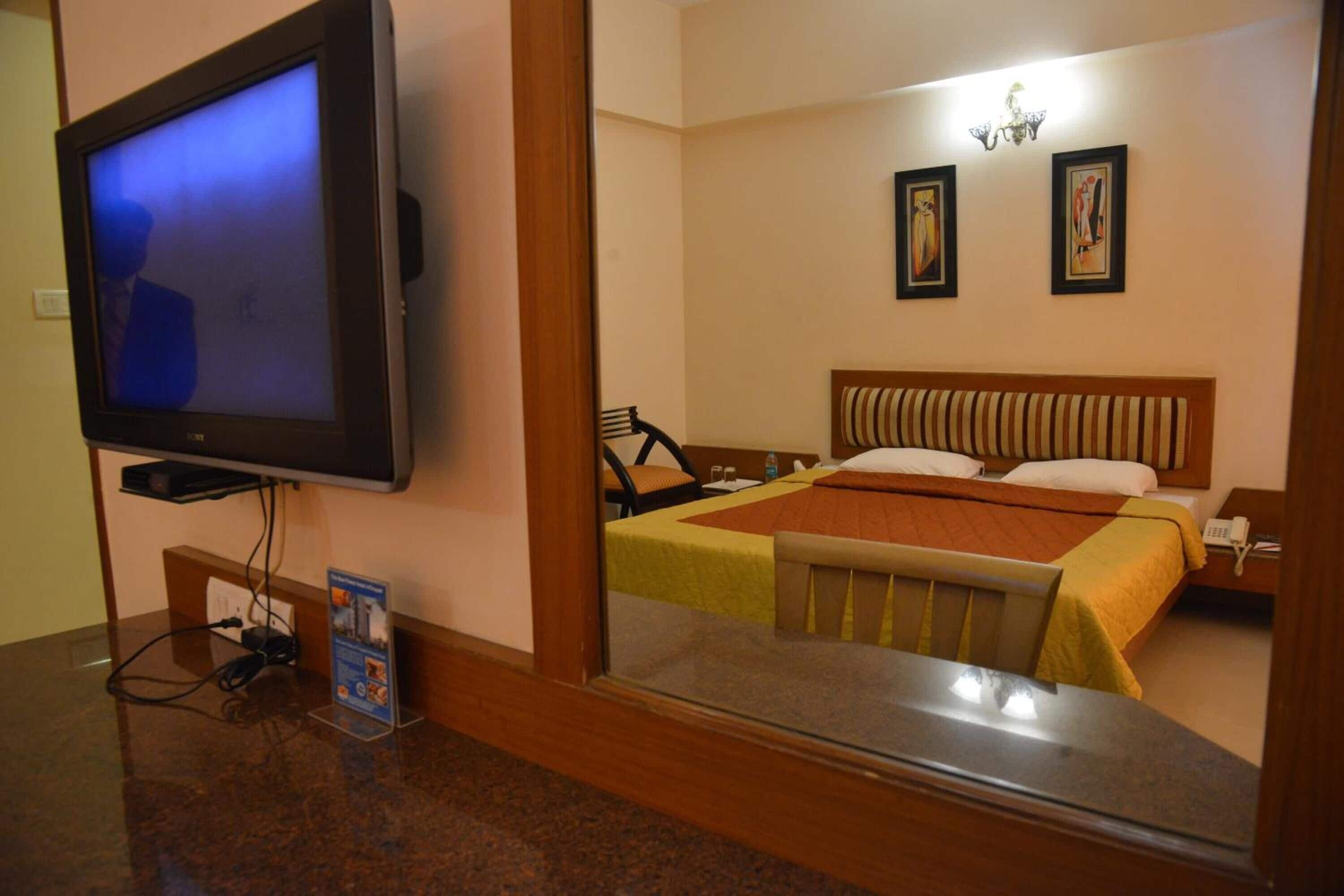 A hotel room with a television, a bed with striped bedding, a nightstand with a phone, and artwork on the wall.