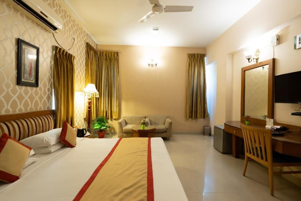 Habitación de hotel con cama, escritorio, silla, sofá, lámpara, planta y ventilador de techo.
