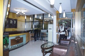 Un área de recepción con un separador de vidrio, un mostrador de recepción, una zona de estar con una mesa de vidrio y una araña.