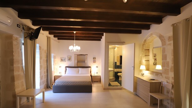 Un dormitorio con cama, mesitas de noche, una banca, escritorio con silla, espejo y candelabro.