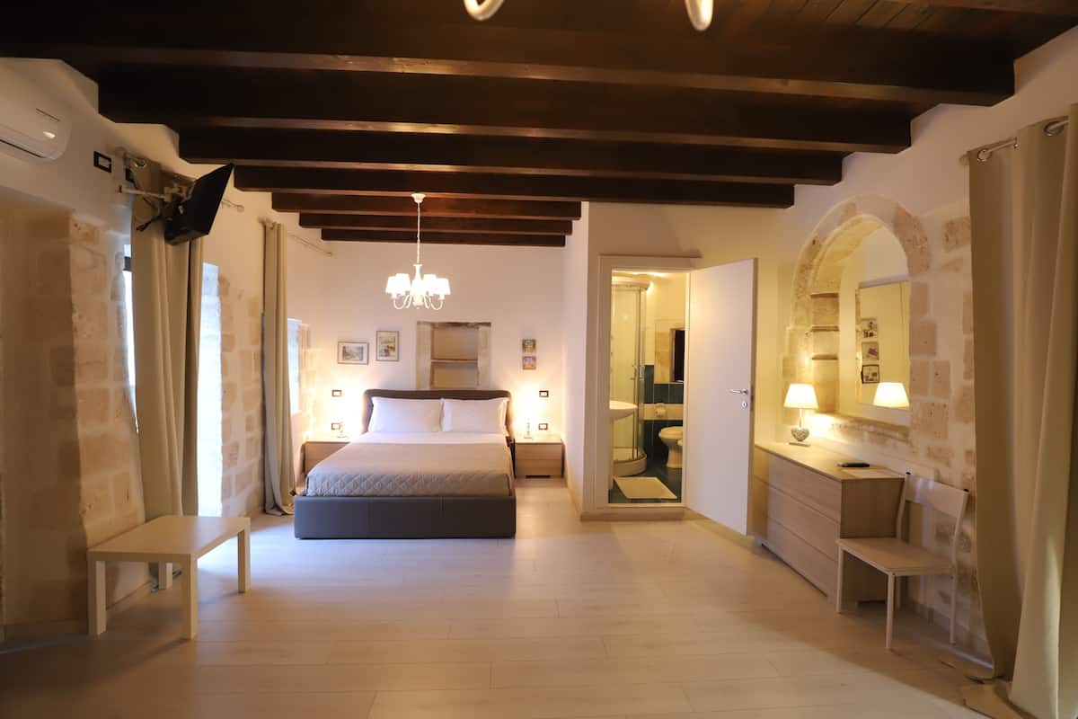 A bedroom with a bed, bedside tables, a bench, a desk with a chair, a mirror, and a chandelier.