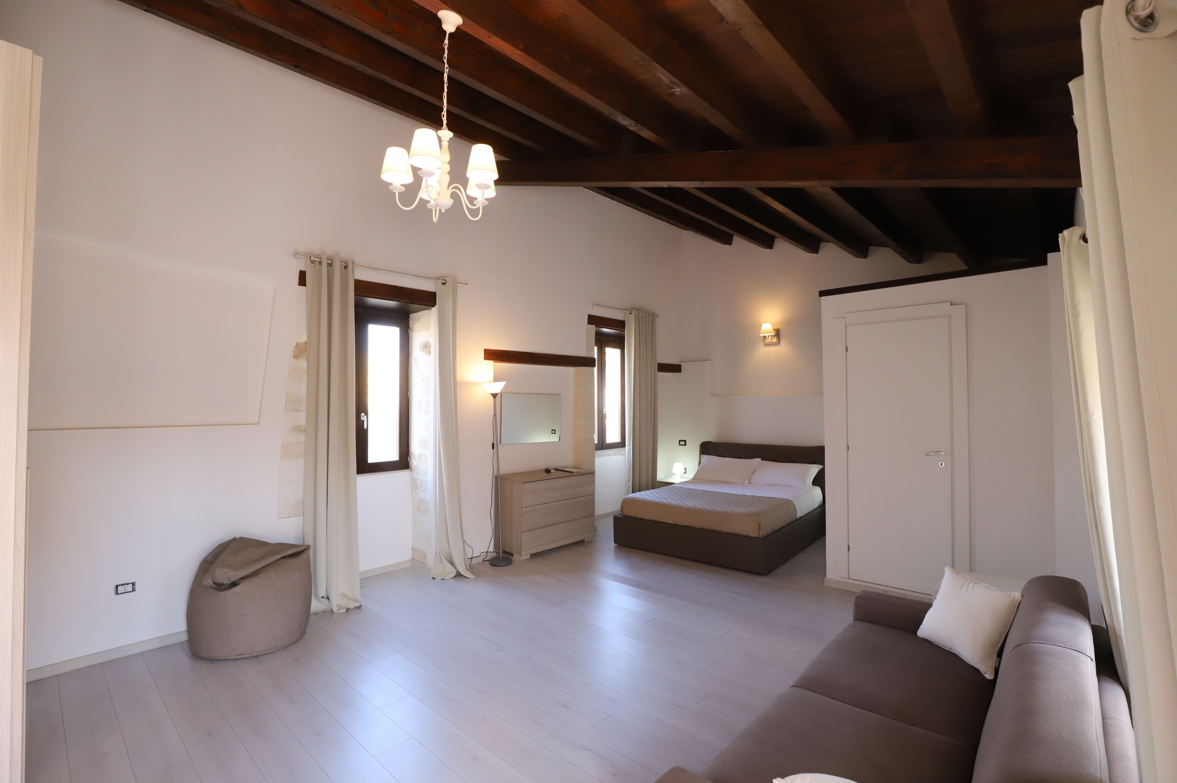 A bedroom with a bed, a bedside table, a dresser, a mirror, and a hanging light fixture.
