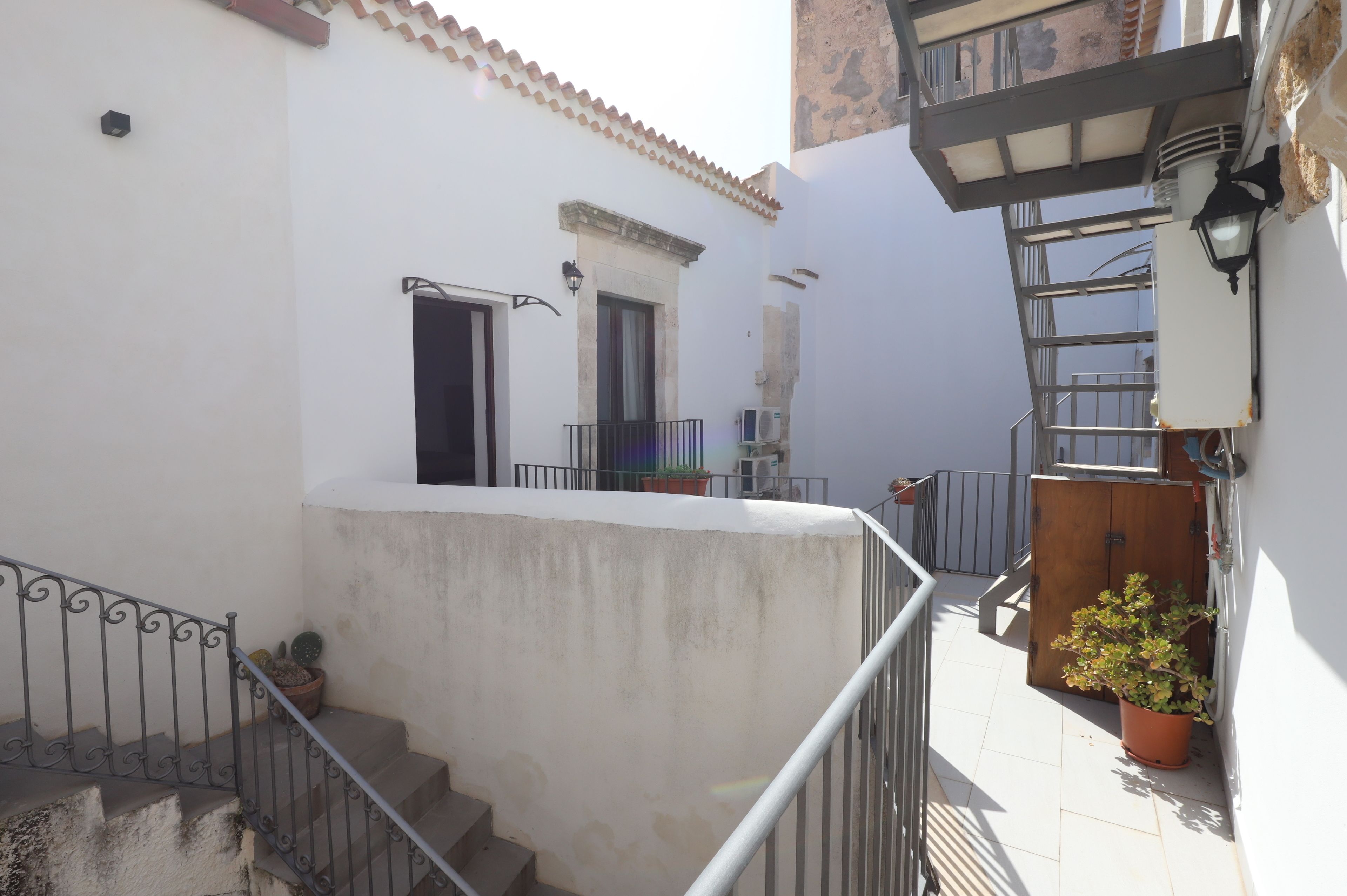 A narrow outdoor corridor with a concrete wall, a metal railing, and a wooden door.