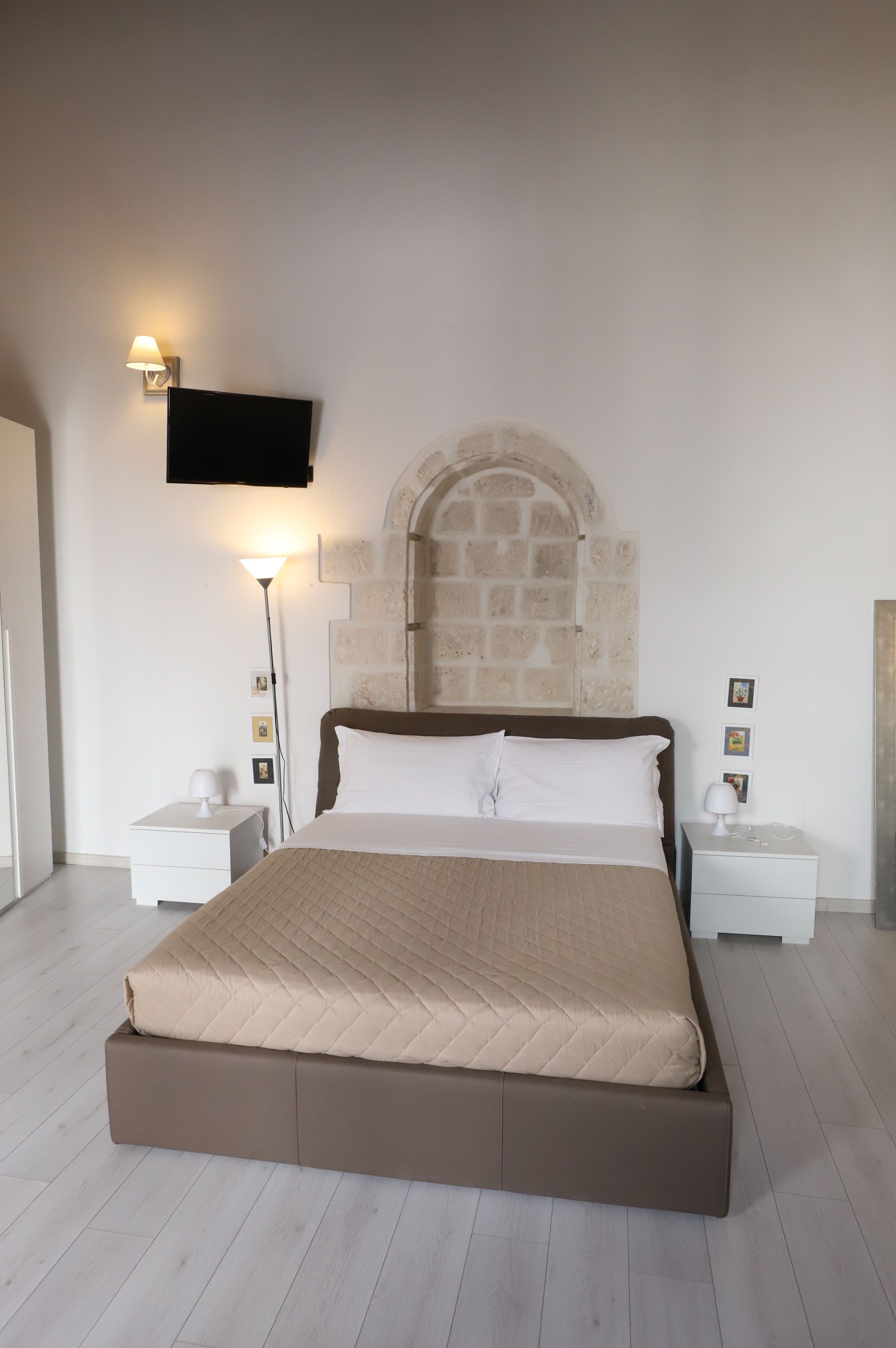 A bedroom with a large bed, a stone wall, a flat-screen TV, and bedside lamps.