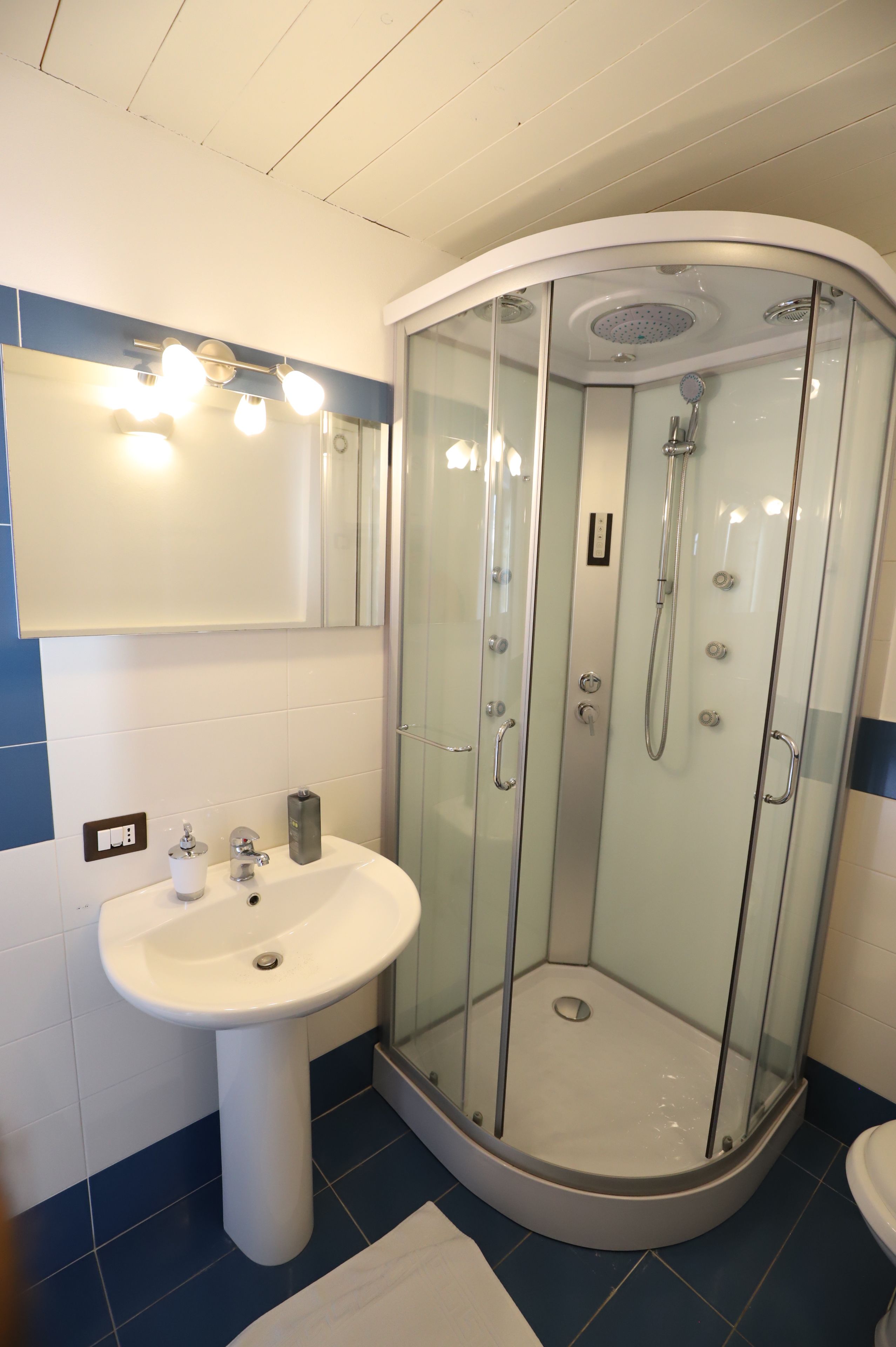 A bathroom with a glass-enclosed shower, a sink, and a mirror with lights.