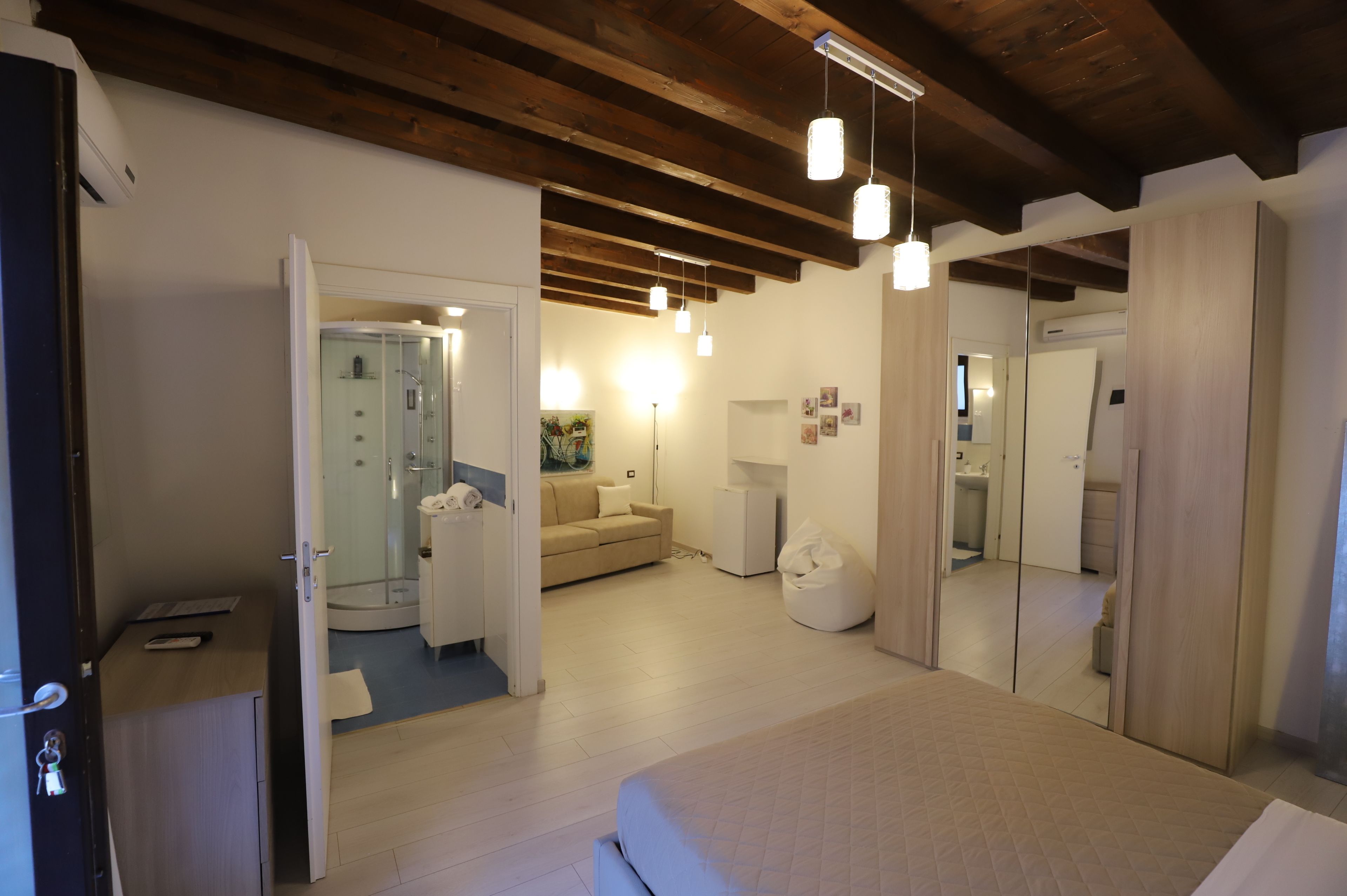Et moderne hotelværelse med en seng, en sofa, brusekabine i glas, et lille bord og et spejl.