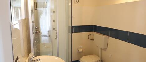 A bathroom with a white sink, two toilets, a glass shower enclosure, and a wooden ceiling.