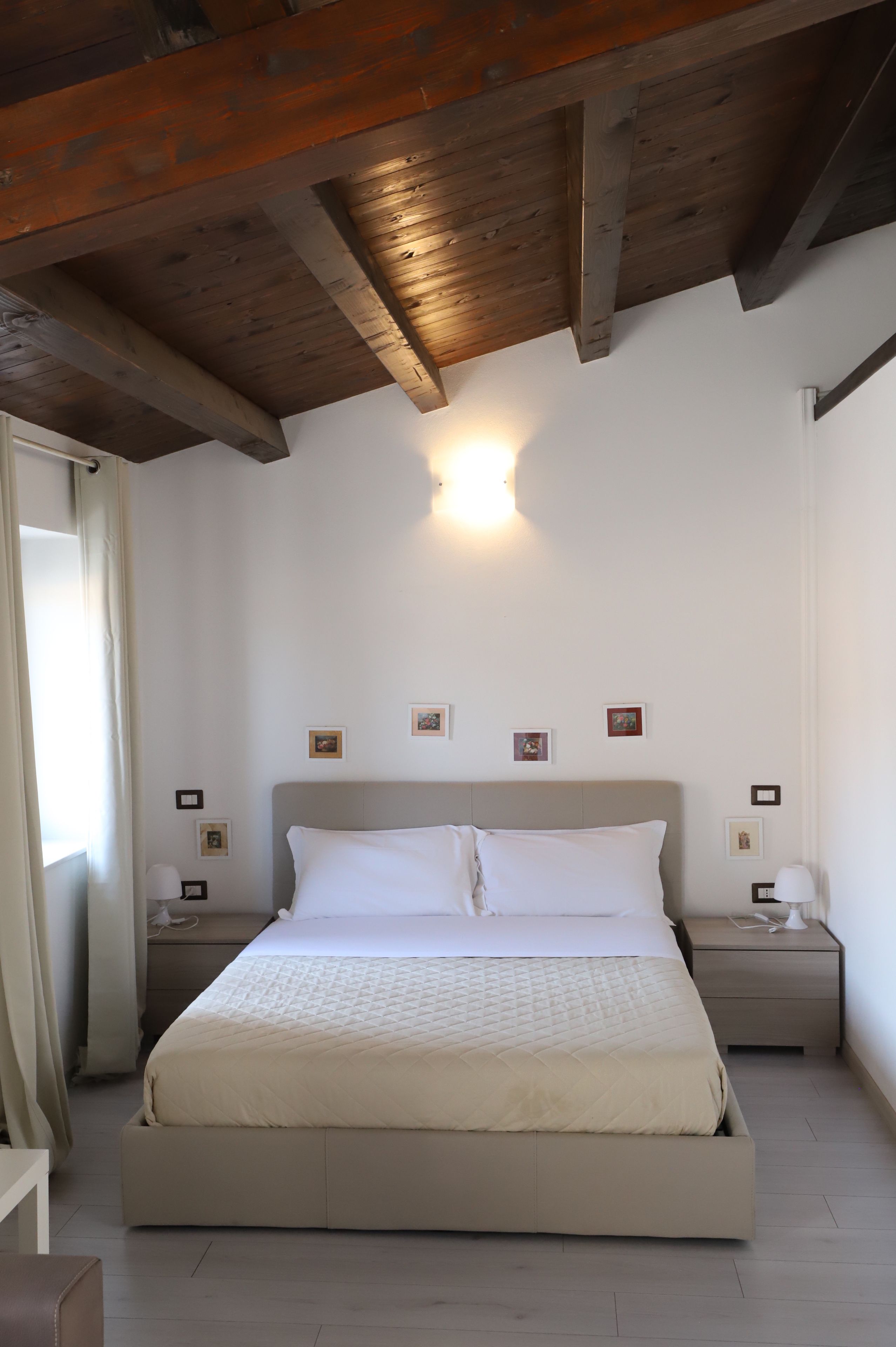 Ein Schlafzimmer mit einem großen Bett, Holzbalken an der Decke, Nachttischen mit Lampen und gerahmten Bildern an der Wand.