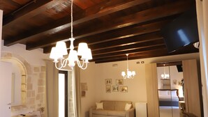 Una habitación amplia con techo de madera alto, un candelabro, un sofá, una mesa de comedor y un televisor.