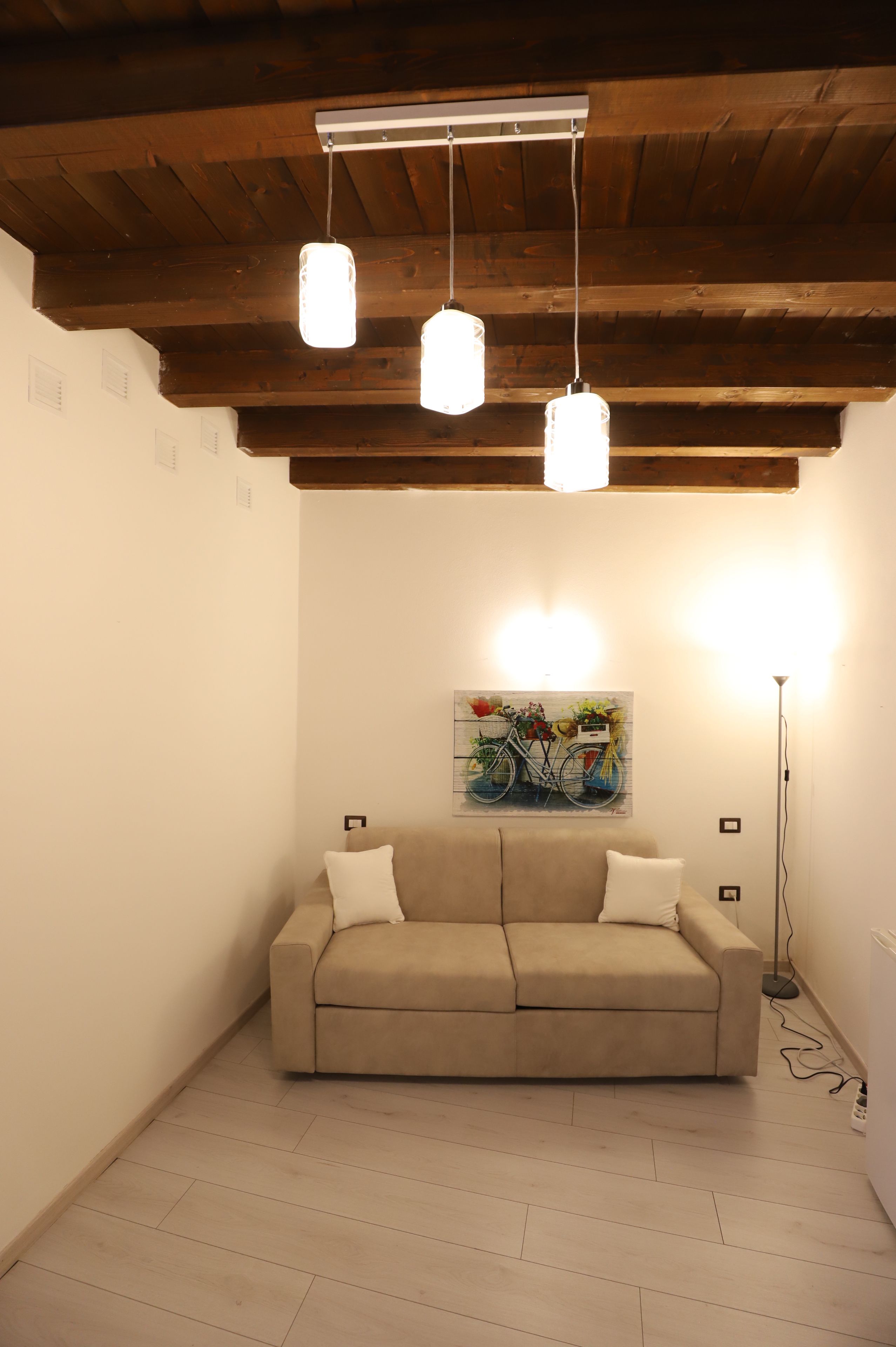 A room with a wooden ceiling, a beige sofa, and a painting of a bicycle.