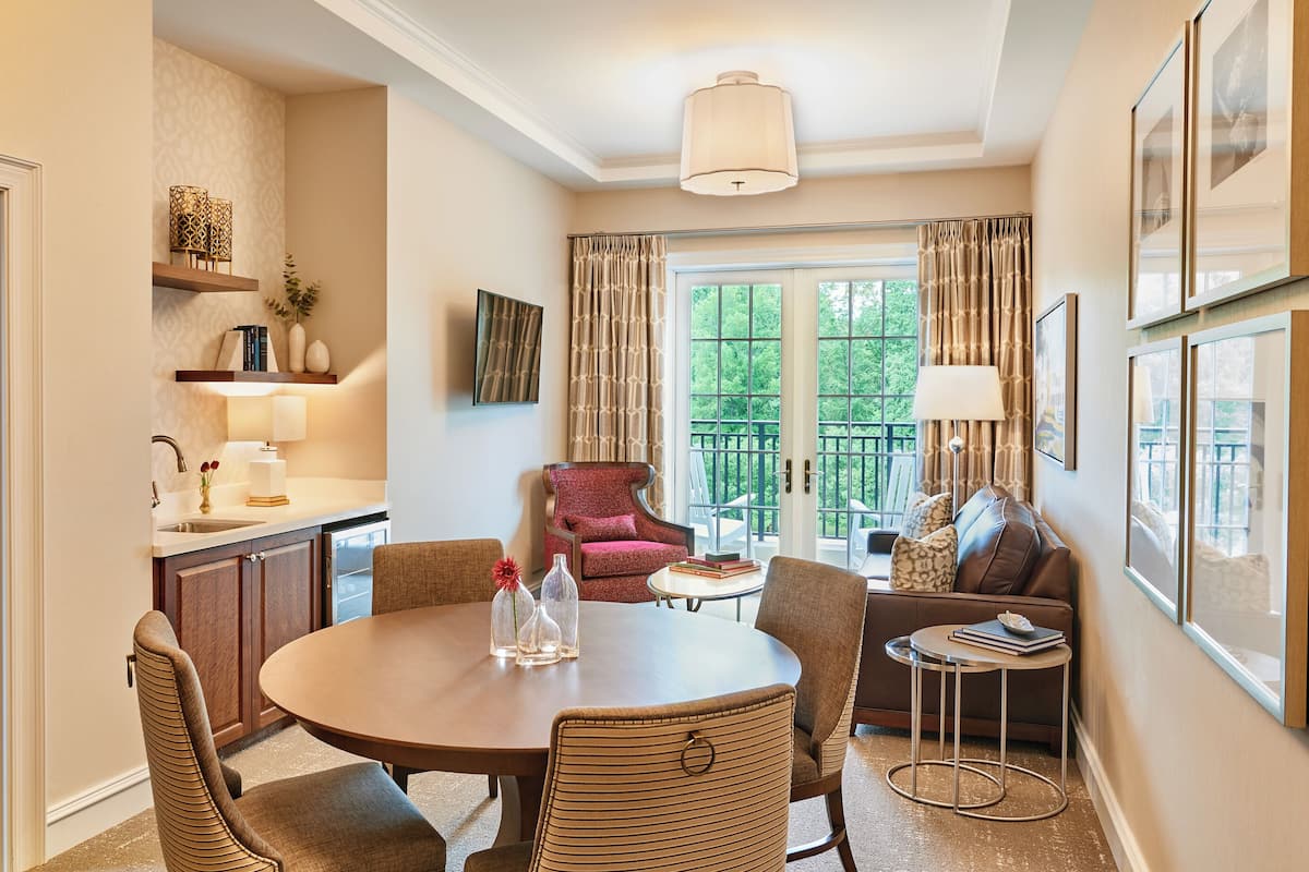 A dining area with a round table, chairs, and a small side table. There is a sofa and a chair in the background.