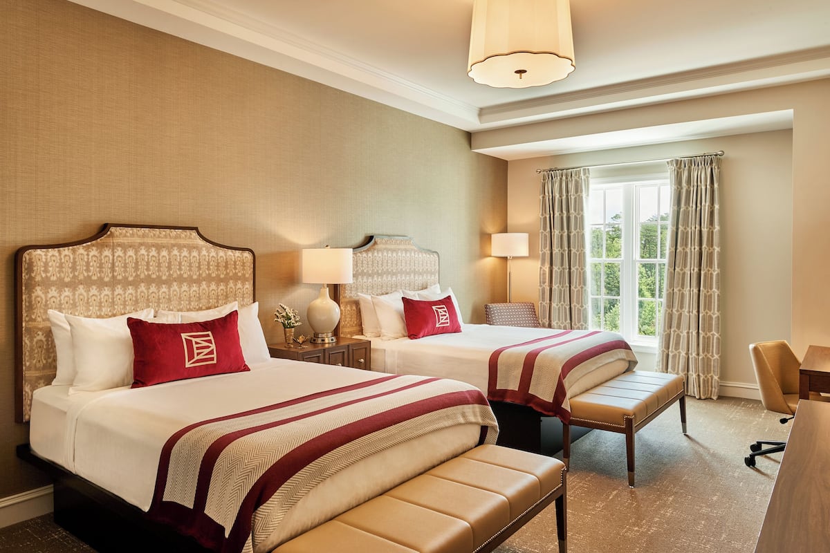 A hotel room with two beds, a bench, a desk, and a chair.