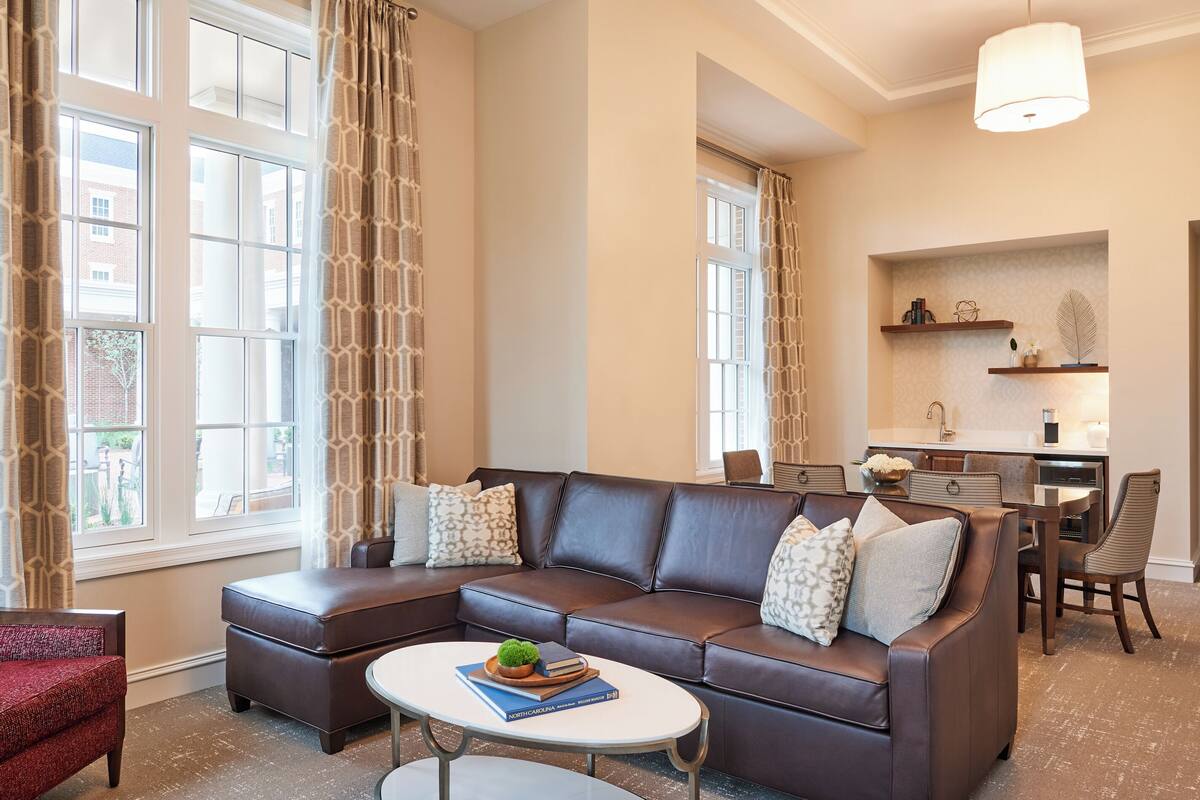 A modern living room with a sectional sofa, a coffee table, and a dining area with a kitchen in the background.