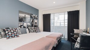 Una habitación de hotel moderna con una cama grande, zona de comedor y vistas a la ciudad a través del ventanal.