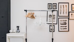 Una habitación blanca con un perchero metálico negro que sostiene ganchos de madera, un candelabro blanco y arte abstracto enmarcado en la pared.