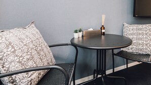 Un rincón de descanso pequeño y moderno con una mesa redonda, dos cojines estampados, una pequeña planta en maceta y un difusor de aroma de juncos.
