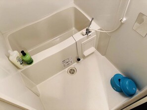 A bathroom with a bathtub, a shower, and a toilet. There are two bottles of shampoo and conditioner on the edge of the bathtub.