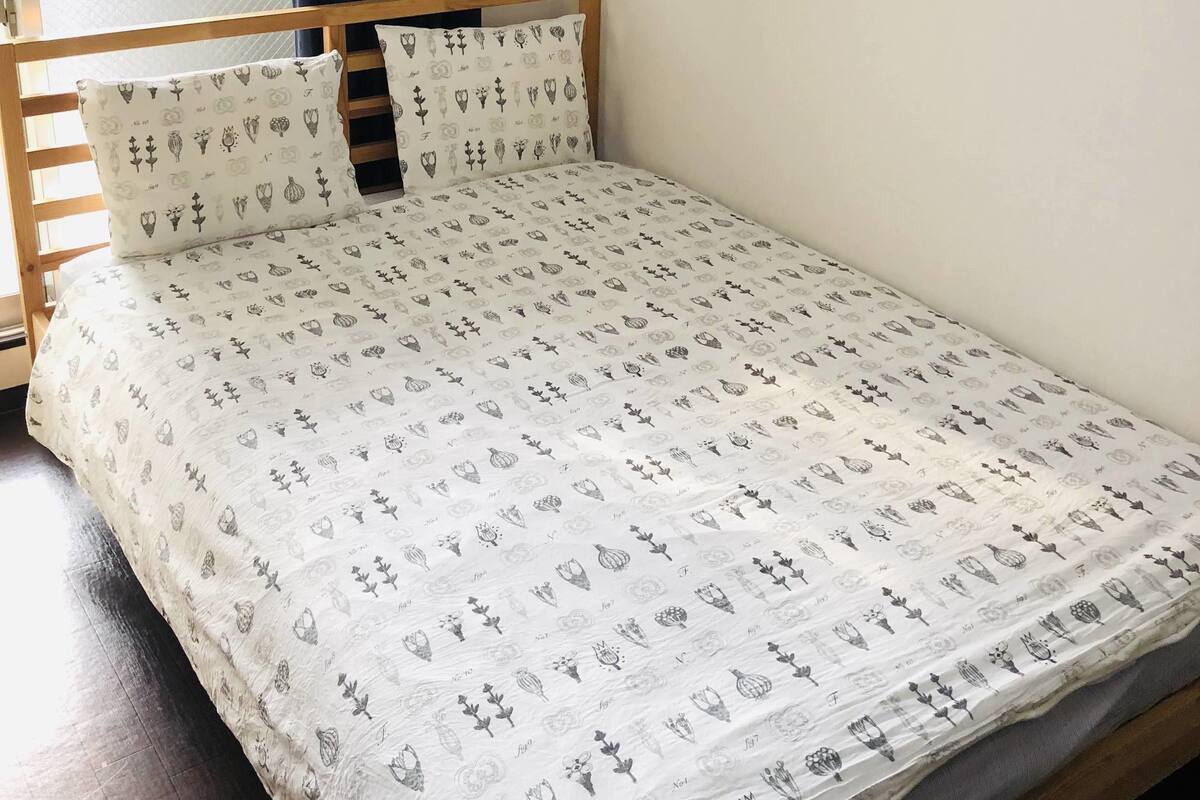 A single bed with a patterned bedspread, a wooden headboard, and a wall-mounted air conditioner.