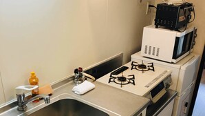 Een kleine keuken met een roestvrijstalen spoelbak, een gasfornuis, een magnetron en een compacte koelkast.
