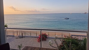 A balcony with a view of the sea, a sandy beach, and a railing.