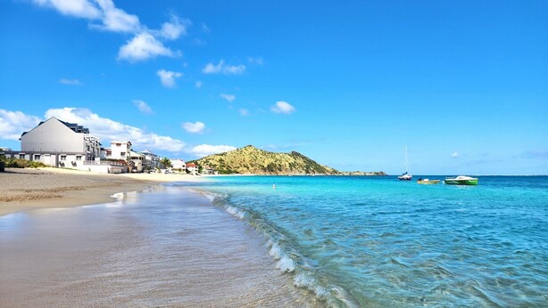 A beach with clear turquoise water, a sandy shore, and a building with a white facade.