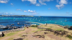 A coastal marina with numerous sailboats docked, a stone wall, and a clear view of the sea.
