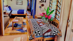 A cozy living room with a sofa, a dining table with a patterned tablecloth, a small table with a notebook, and a chair.